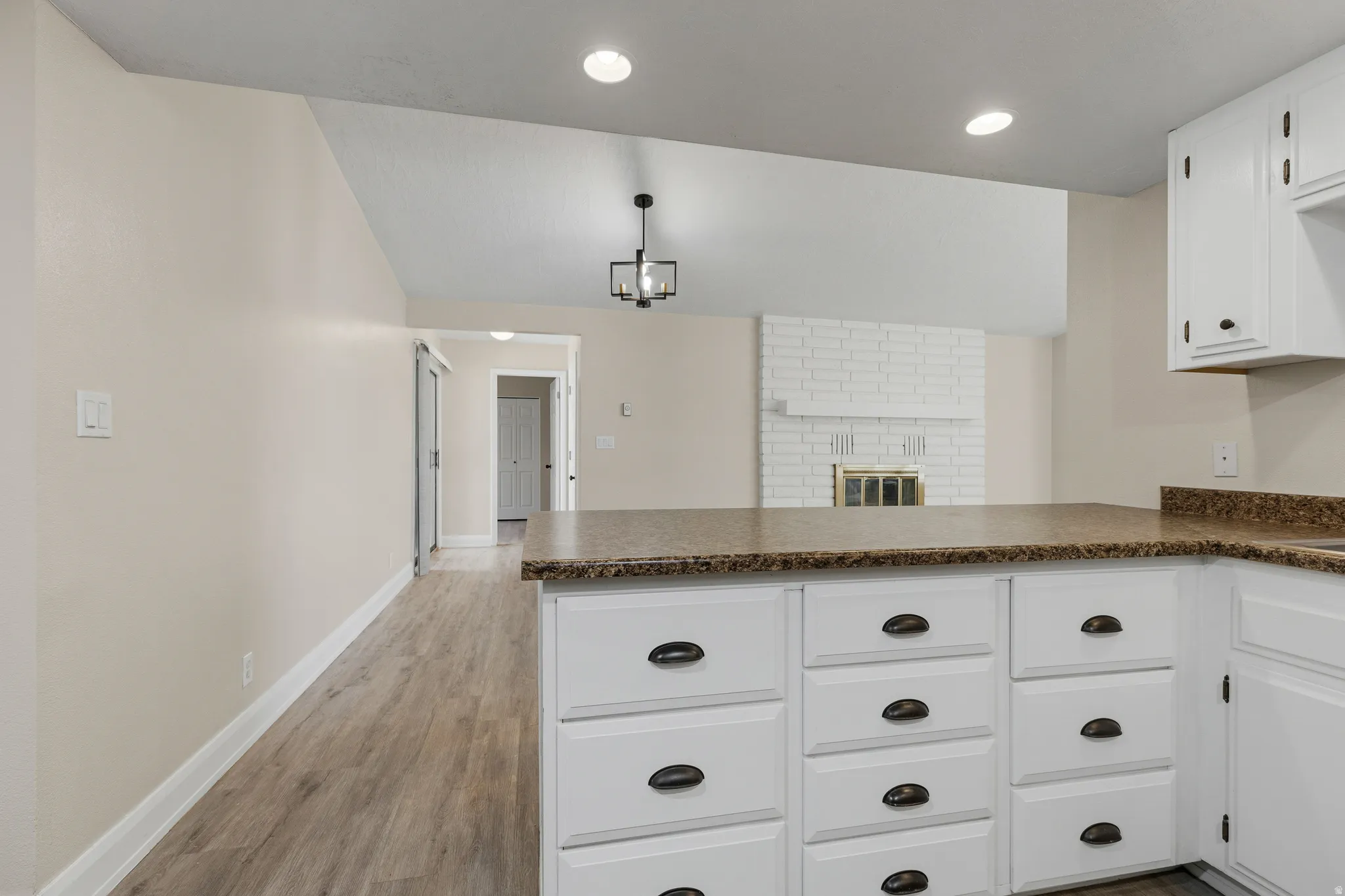 Kitchen island with white cabinetry and dark hardware, wood-finish flooring, and vaulted ceiling