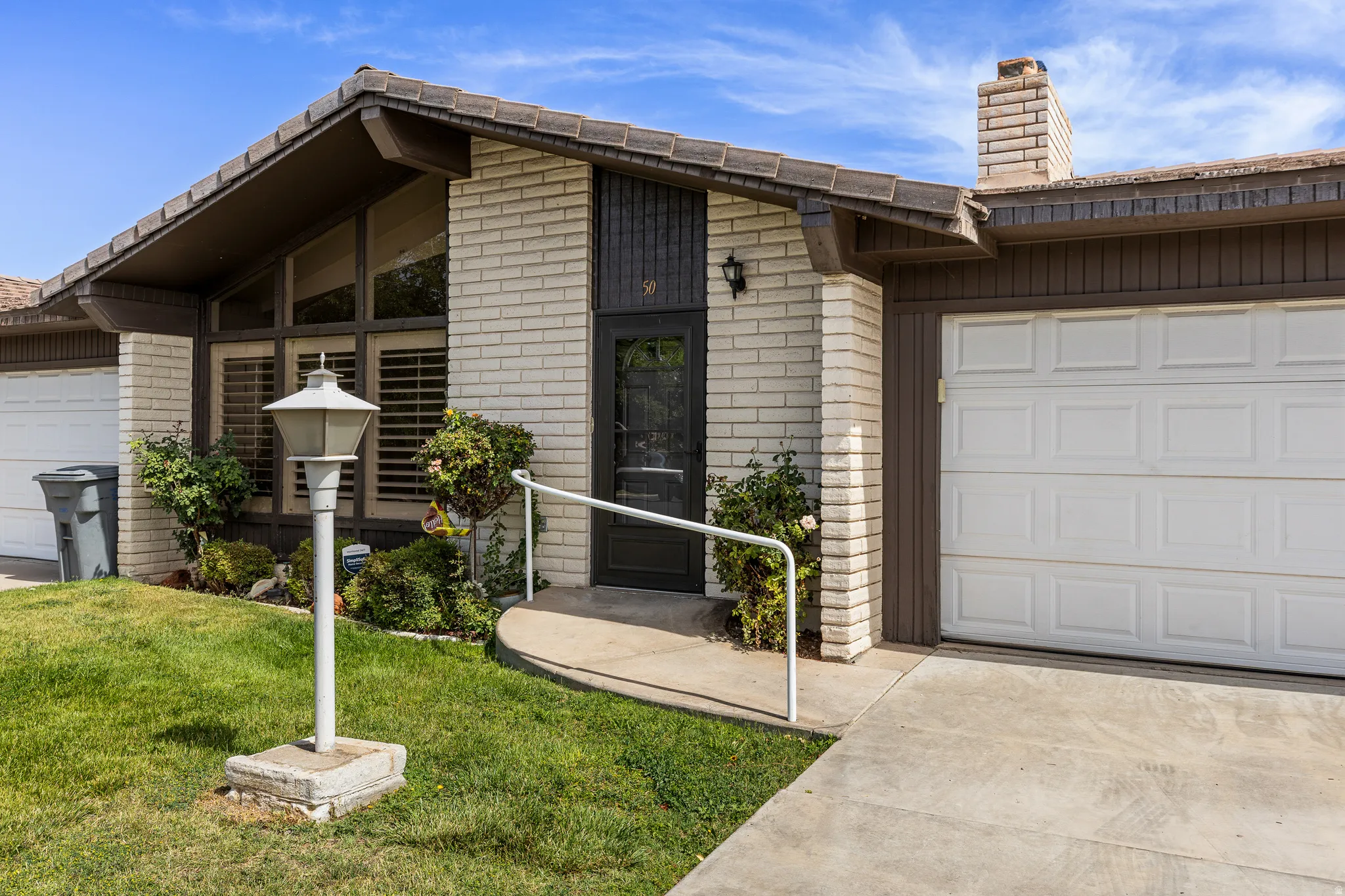Brick exterior with a gabled roofline, integrated garage, front entry with handrail, and front yard landscaping
