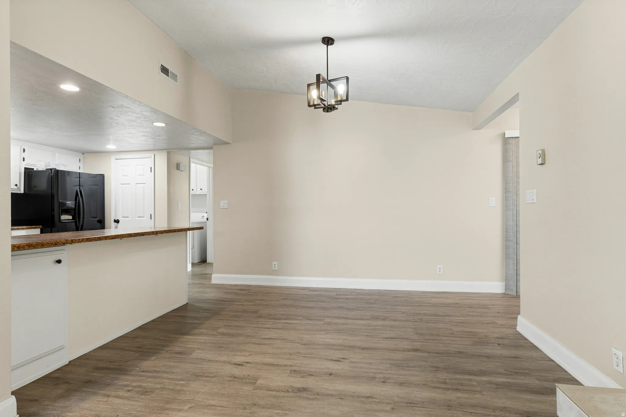 Vaulted ceiling with a contemporary chandelier, wood-finish flooring, and a kitchen pass-through with a stone-finish countertop