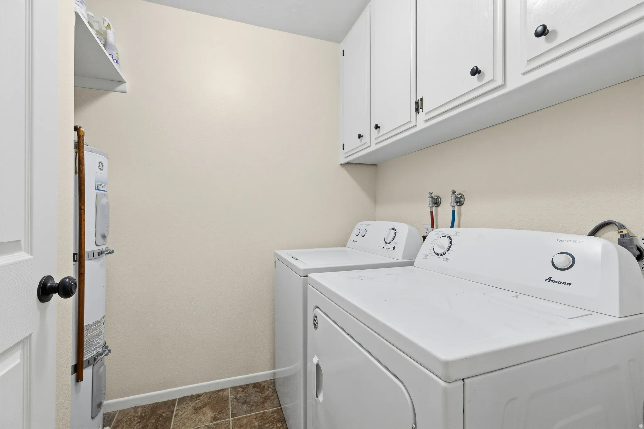 White upper cabinetry with black hardware, white appliances, wall-mounted connections, and tiled flooring