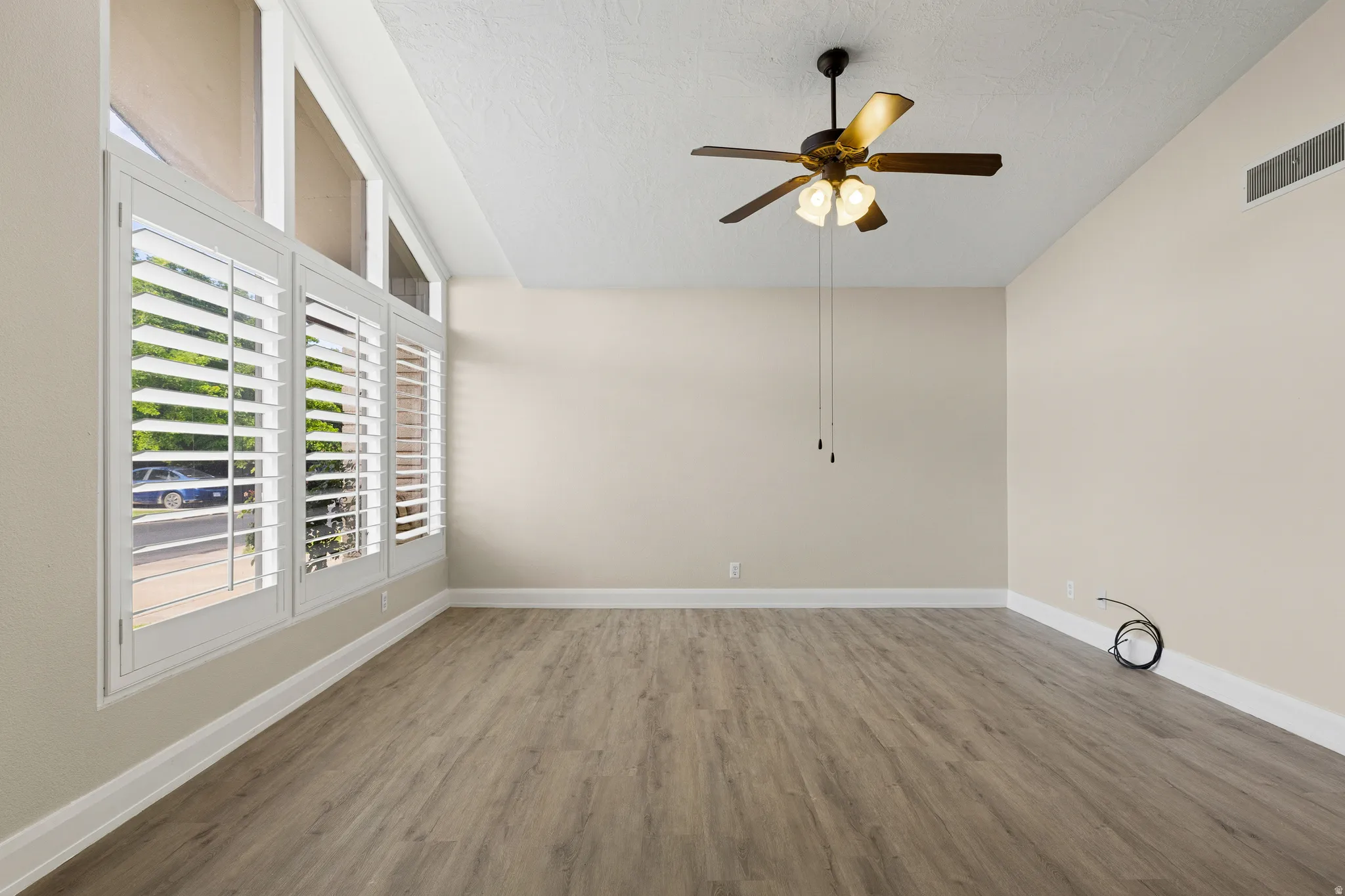Vaulted ceiling with a ceiling fan, wood-finish flooring, and white window shutters