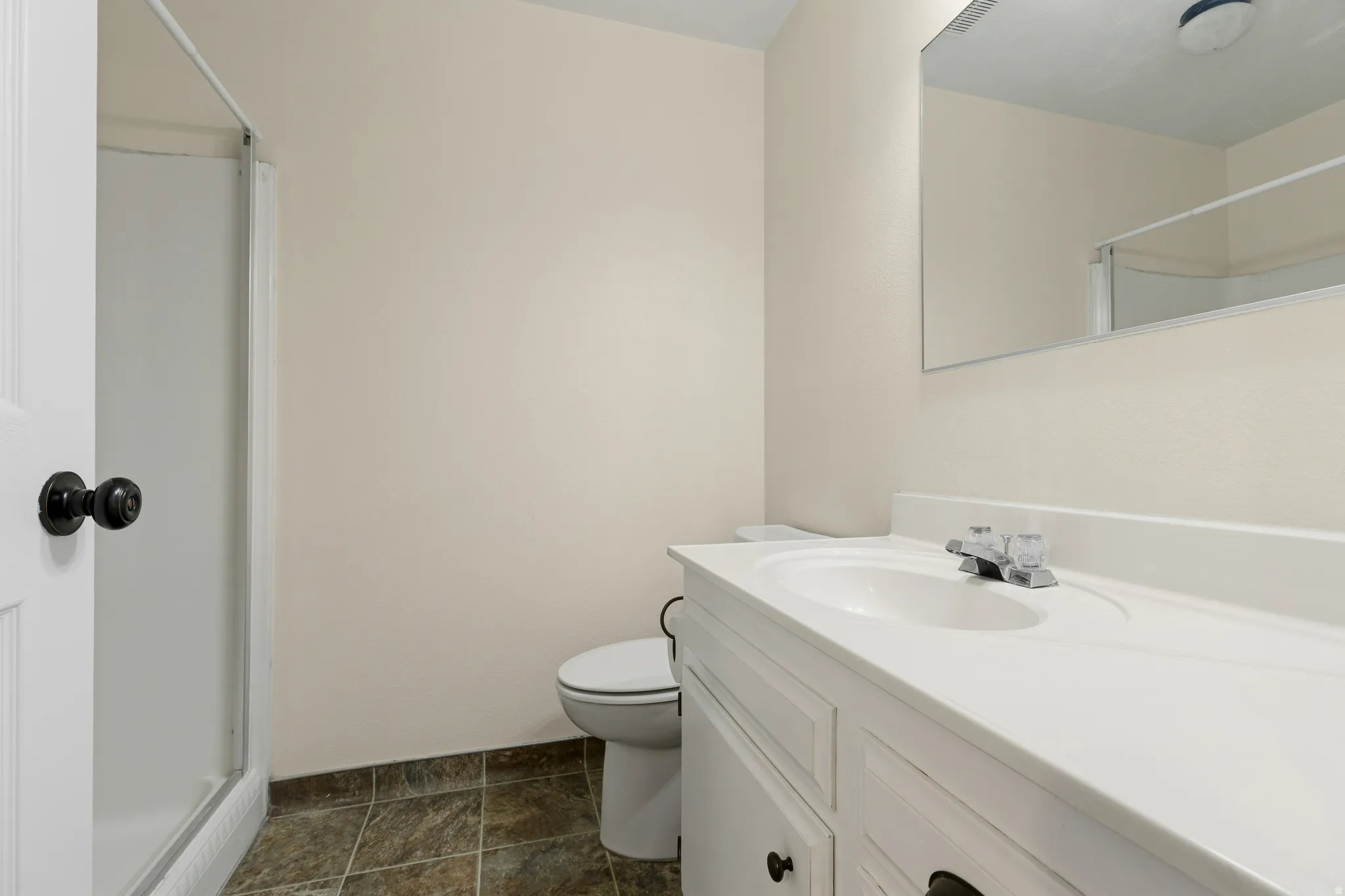 Bathroom featuring a shower enclosure, vanity with integrated sink, chrome faucet, wall-mounted mirror, and tile flooring