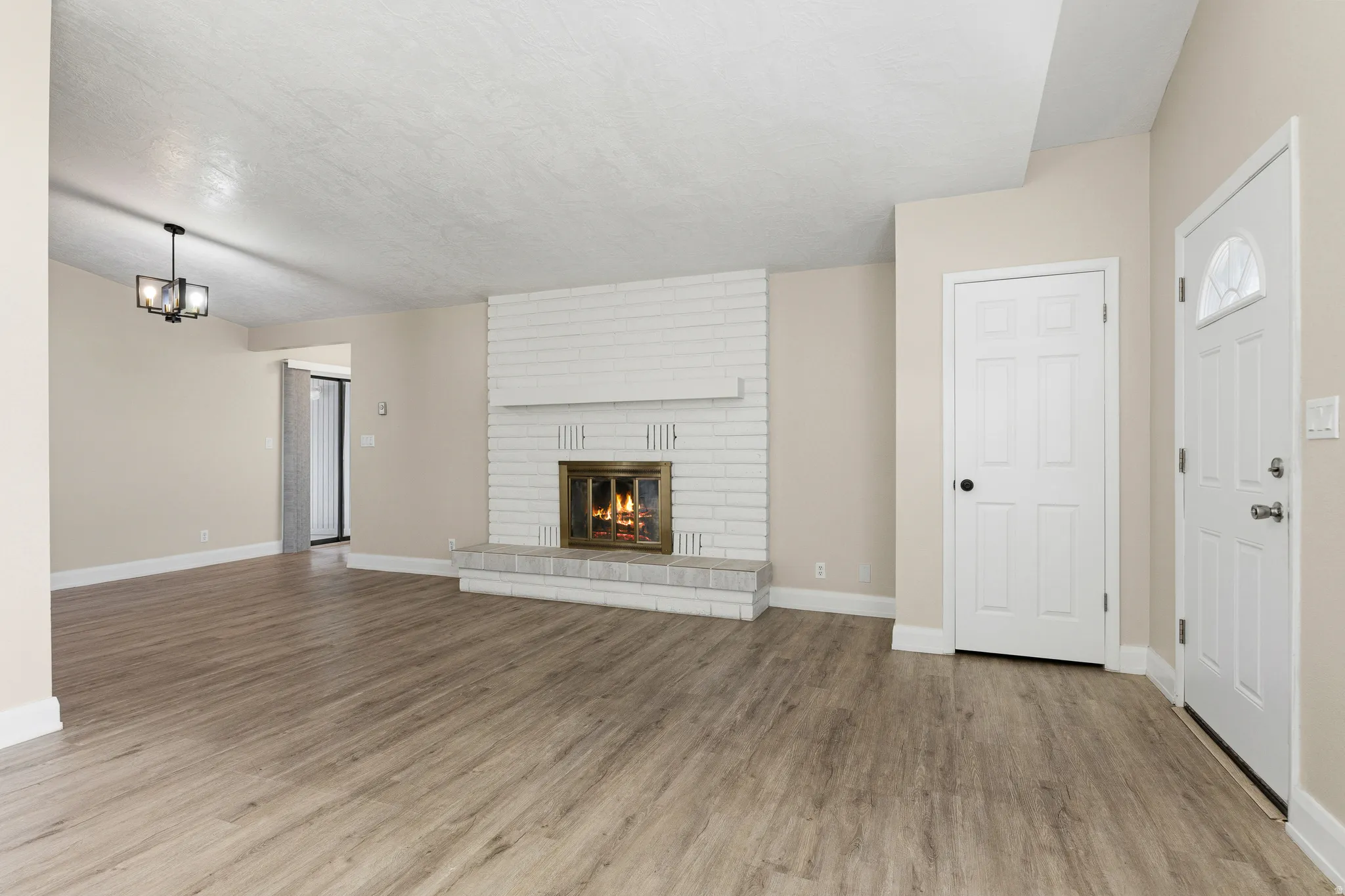 Wood-finish flooring, white brick fireplace with hearth, white paneled interior door, and a front entry door with an arched glass insert
