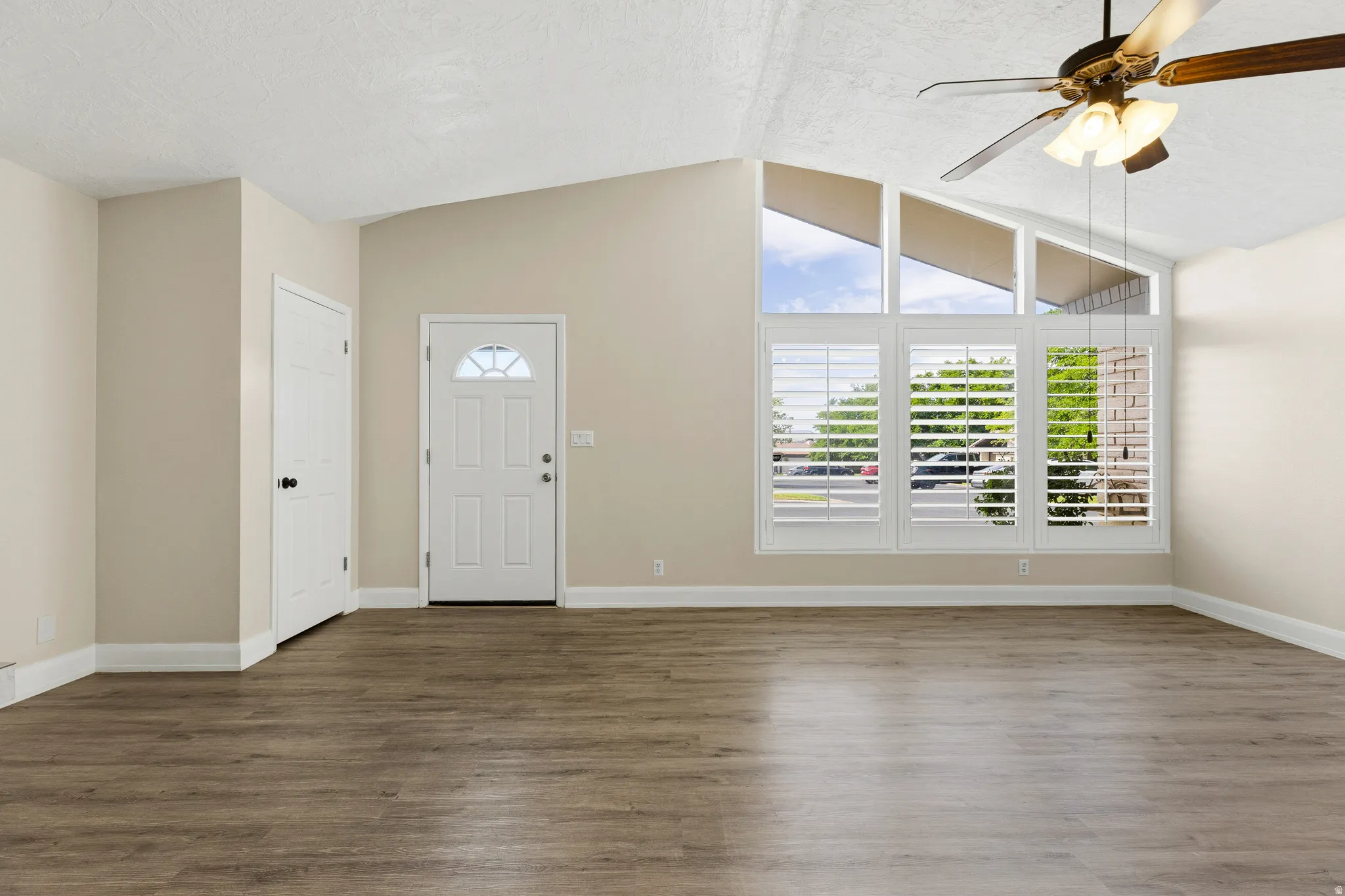 Vaulted ceiling with a ceiling fan, wood-finish flooring, plantation shutters, and a front entry door with an arched transom window