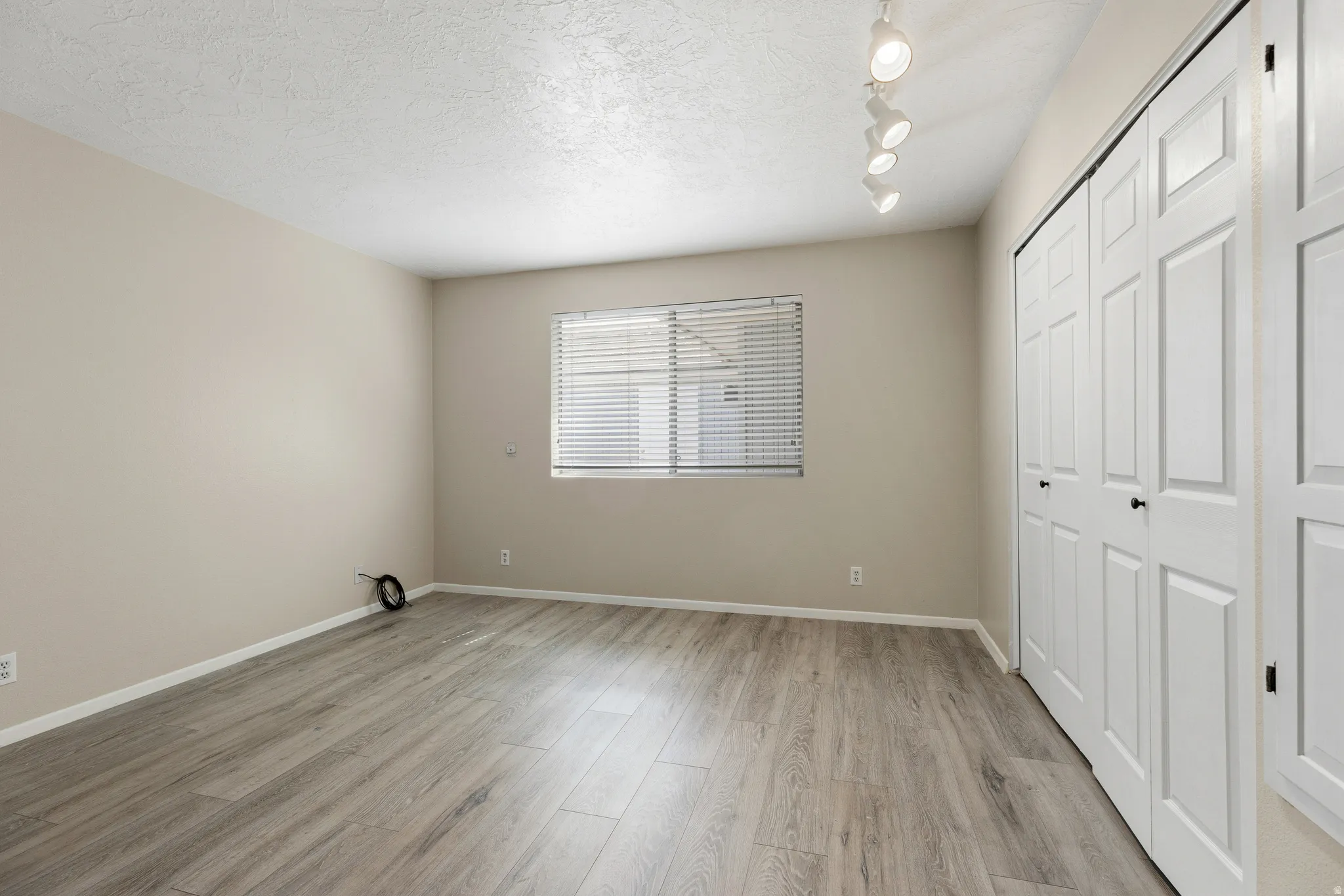 Wood-finish flooring, neutral wall tones, window with horizontal blinds, track lighting, and bi-fold closet doors