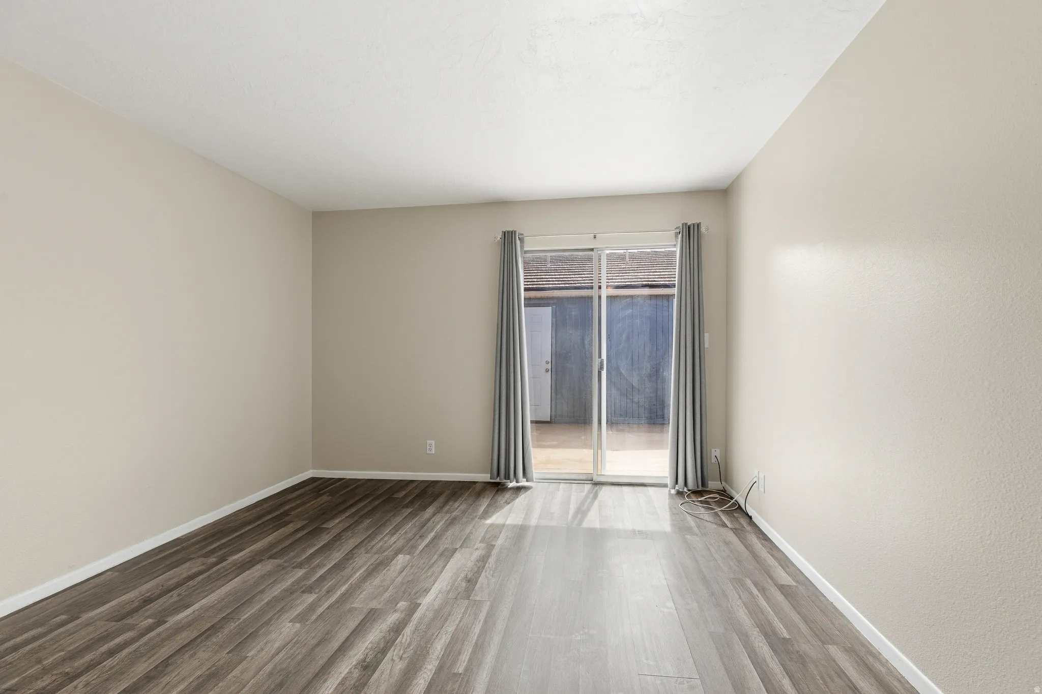 Sliding glass door, wood-finish flooring, light-toned walls, and neutral curtains