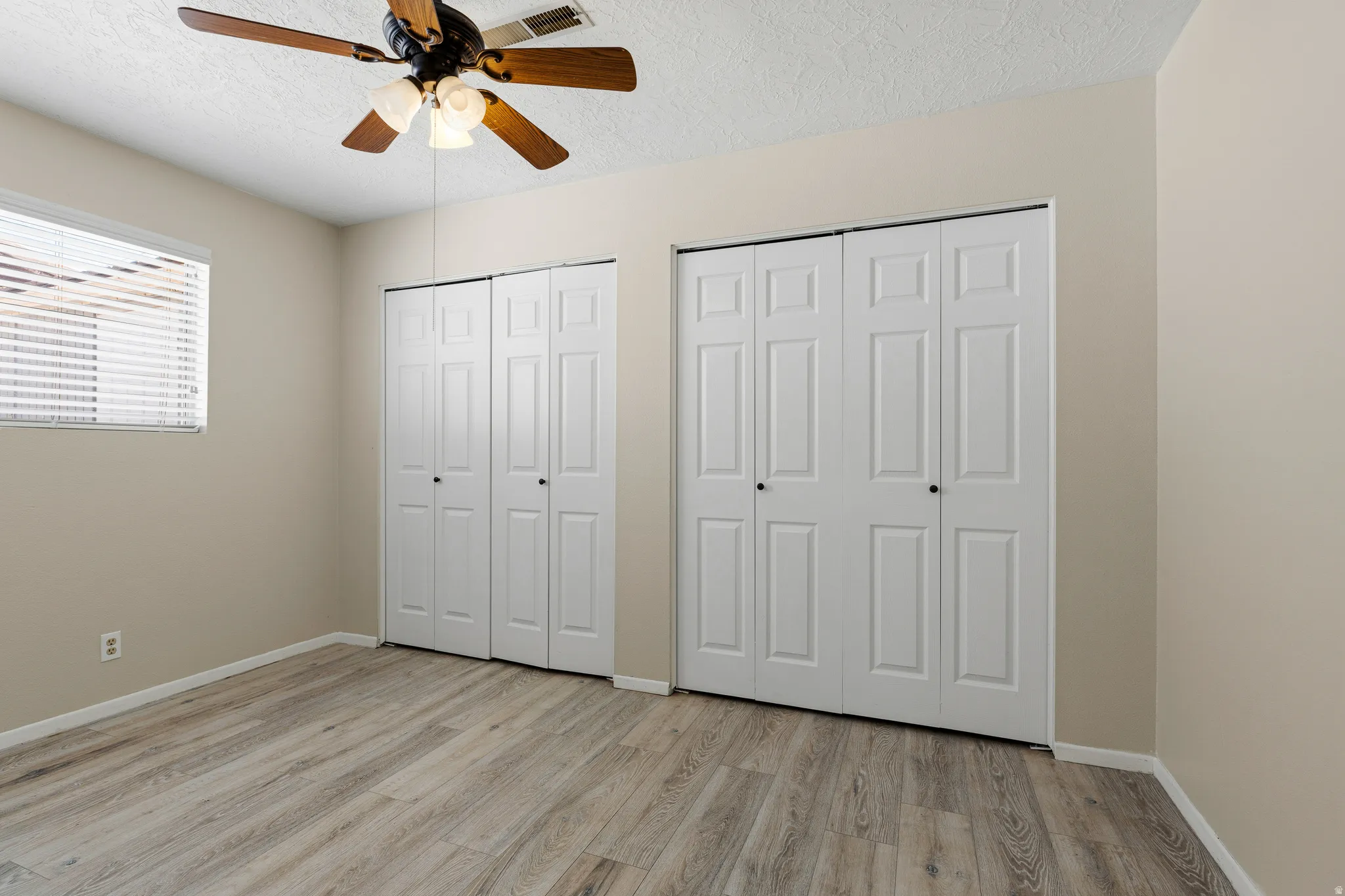 Wood-finish flooring, ceiling fan with integrated lighting, window with blinds, and dual bi-fold closet doors
