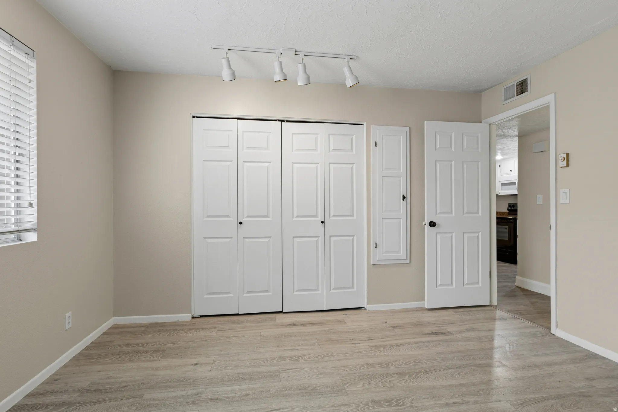Wood-finish flooring, neutral paint, track lighting, paneled doors, and window with blinds