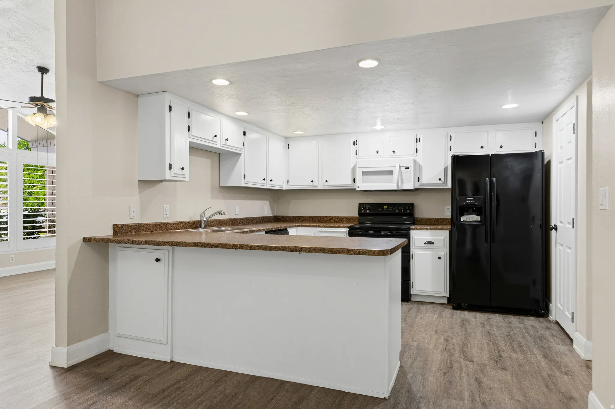 U-shaped kitchen featuring white cabinetry, dark countertops, a built-in microwave, and a black refrigerator