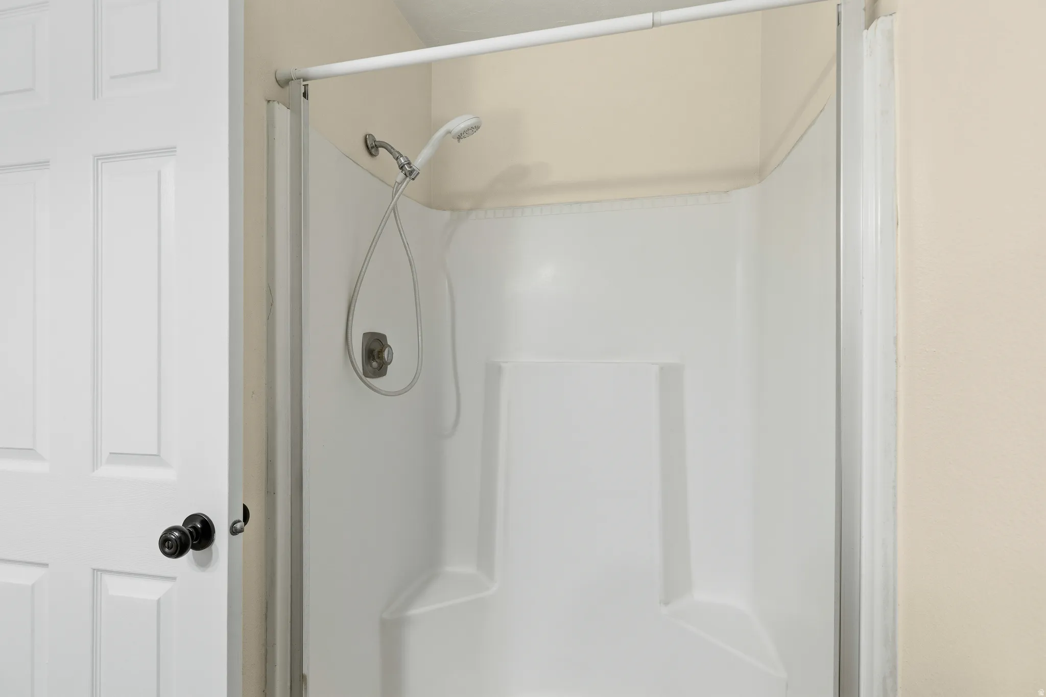 White shower enclosure with integrated shelving and a handheld shower fixture