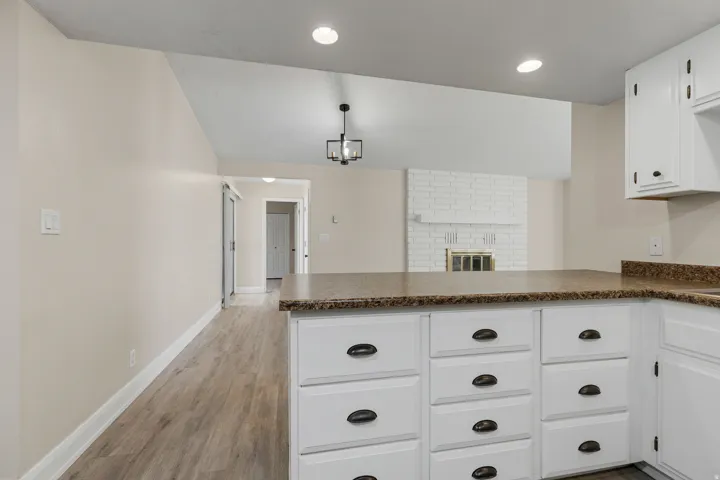 Kitchen island with white cabinetry and dark hardware, wood-finish flooring, and vaulted ceiling