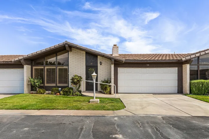 Brick façade with a gabled roofline, expansive front windows, attached two-car garage, and established landscaping