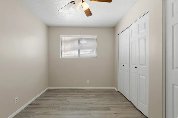 Wood-finish flooring, neutral wall tones, white blinds, and a ceiling fan with light fixture