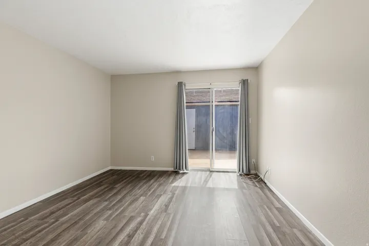 Sliding glass door, wood-finish flooring, light-toned walls, and neutral curtains