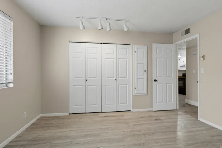 Wood-finish flooring, neutral paint, track lighting, paneled doors, and window with blinds