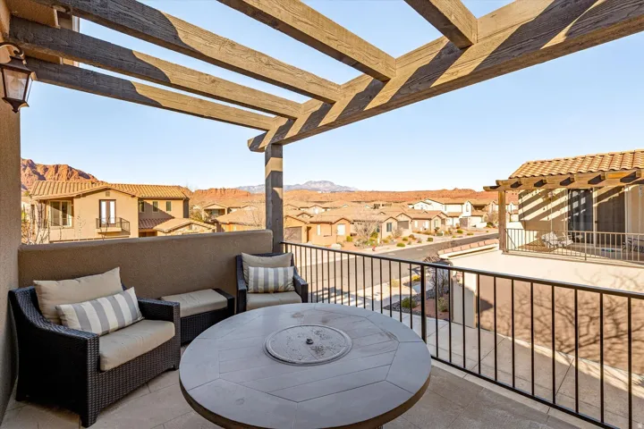 Outdoor balcony featuring a wood-beam pergola, stucco privacy wall, and black metal railing