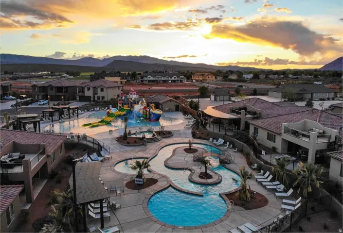 Community pool area featuring multiple swimming areas, a water park structure, and surrounding residential buildings with mountain backdrop