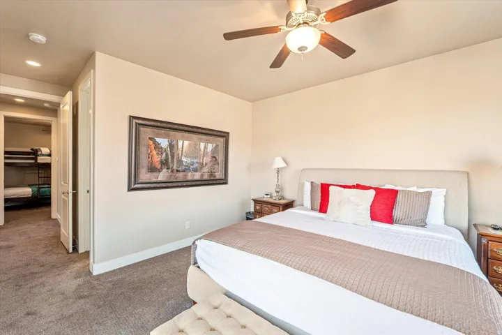 Plush carpet flooring, ceiling fan, and a light-toned upholstered headboard