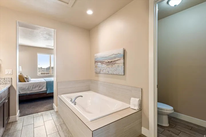 Built-in soaking tub with tile surround, wood-finish tile flooring, recessed lighting, and a separate water closet