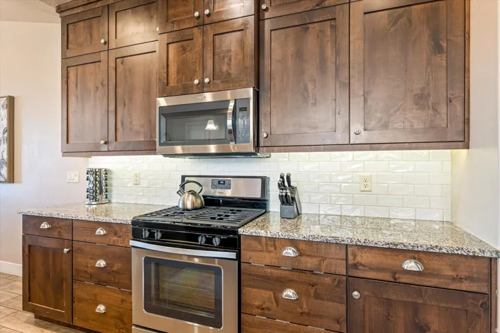 Dark wood-finish cabinetry with modern hardware, speckled countertops, stainless steel range, and built-in microwave
