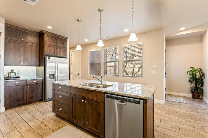 Kitchen featuring wood-finish cabinetry, stainless steel appliances, a center island with double sink, granite countertops, and tile flooring
