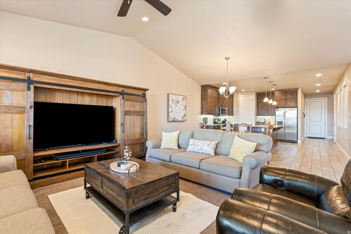 Vaulted ceiling with recessed lighting, integrated wood-finish entertainment center with barn door accents, open-concept design, and a kitchen with dark wood-finish cabinetry and stainless steel appliances