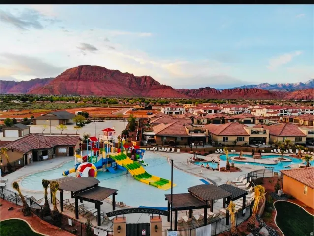 Expansive community pool area featuring multiple swimming zones, water slides, and shaded cabanas