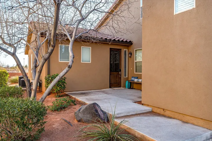 Stucco exterior with a tile roof, an inviting covered entryway, a wood-panel front door, and established landscaping