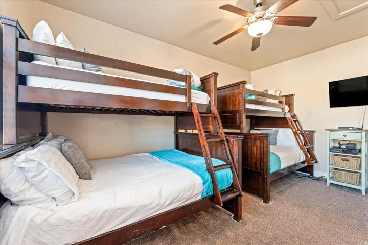 Bedroom featuring two bunk beds with integrated ladders, a ceiling fan with light fixture, and carpeted flooring