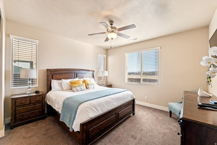 Carpeted bedroom with a ceiling fan light fixture and multiple windows