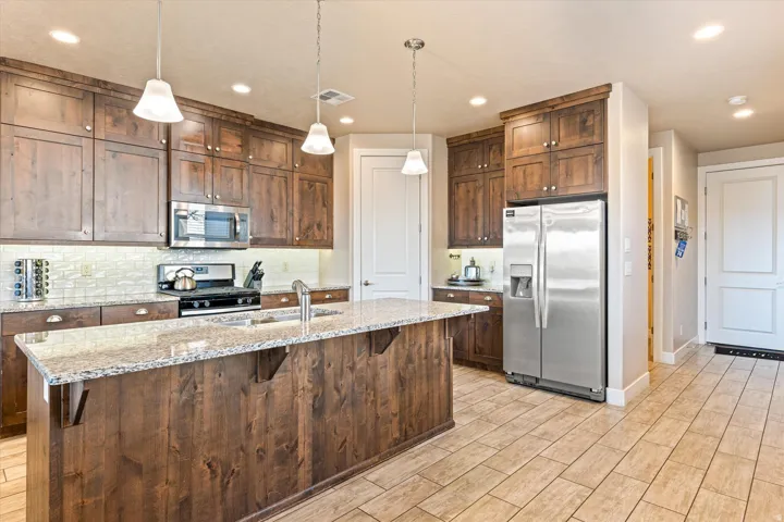 Spacious kitchen featuring dark wood cabinetry, stainless steel appliances, a large island with a light-toned countertop, and recessed lighting