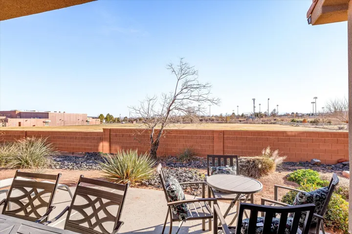Paved patio area, low-maintenance landscaping, brick perimeter wall, clear sky backdrop, distant open fields