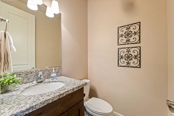 Granite countertop with an undermount sink, wood-finish vanity, wall-mounted mirror, and a three-light vanity fixture