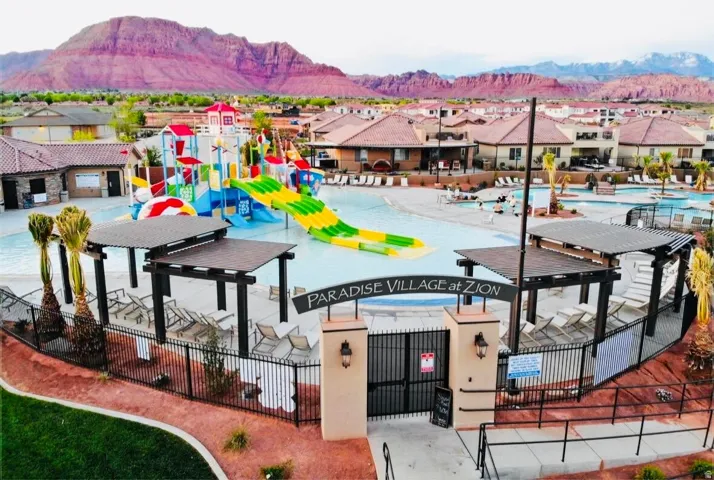 Paradise Village at Zion entrance featuring a large pool area with water slides, multiple shade structures, and surrounding residential buildings with tile roofs