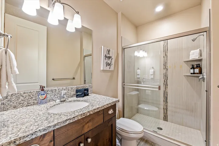 Granite-style countertop with an integrated sink, wood-finish vanity with drawer storage, framed glass shower enclosure, and tiled shower with built-in shelving