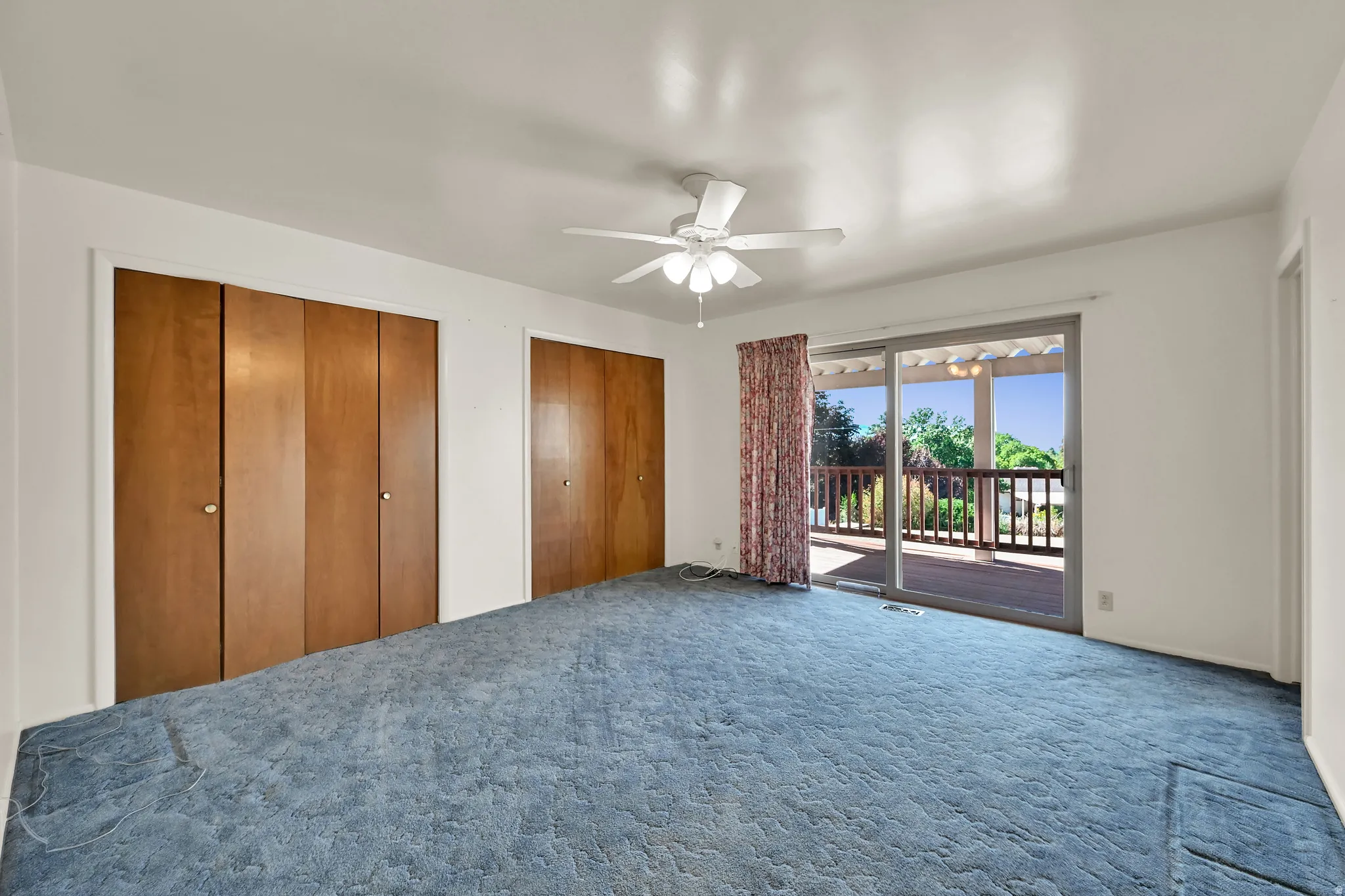 Expansive room with built-in wooden closet doors, a ceiling fan, and sliding glass doors leading to an outdoor deck featuring wood railings and a pergola