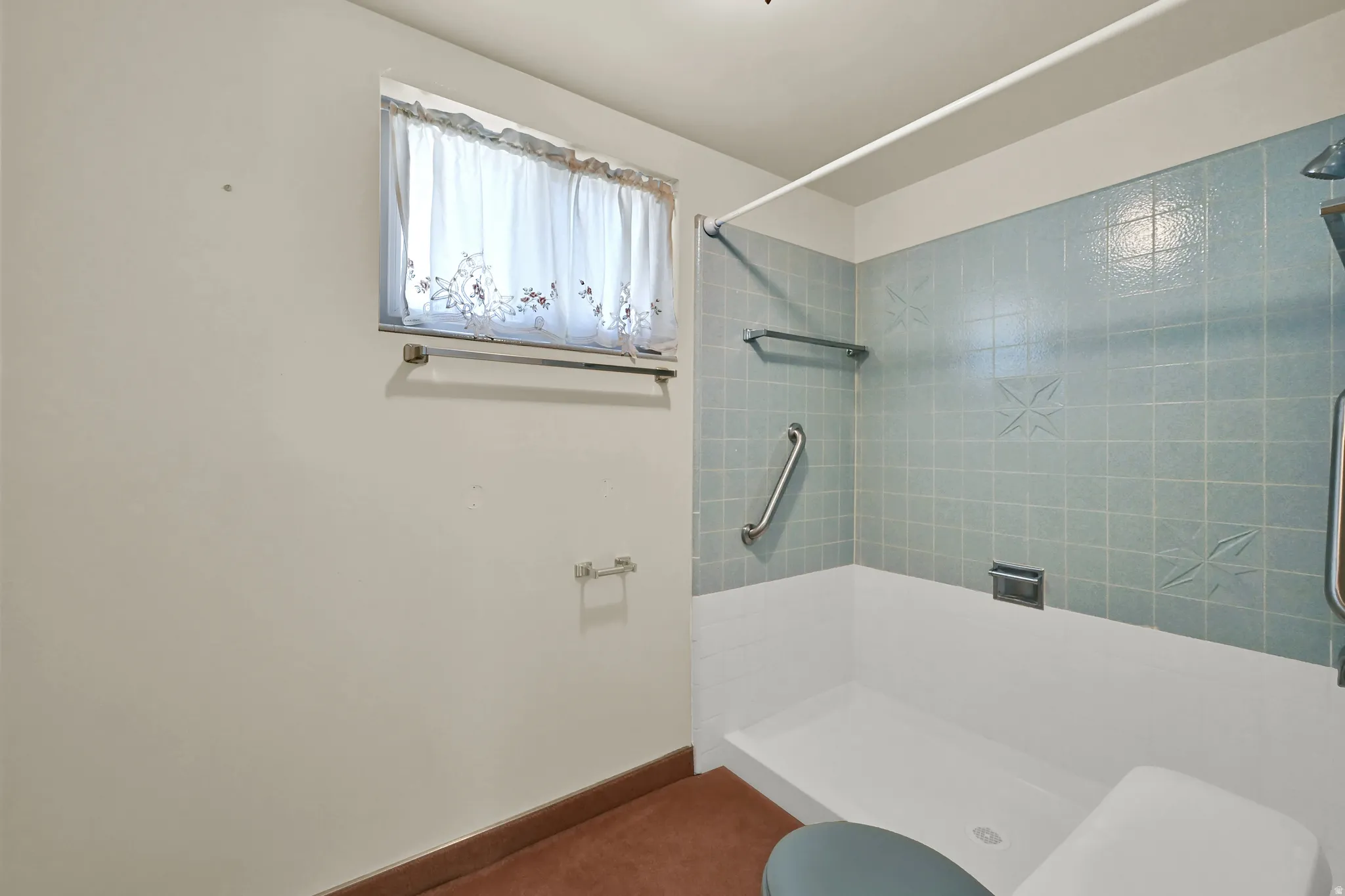 Shower with blue tile surround, built-in grab bars, and a white shower pan