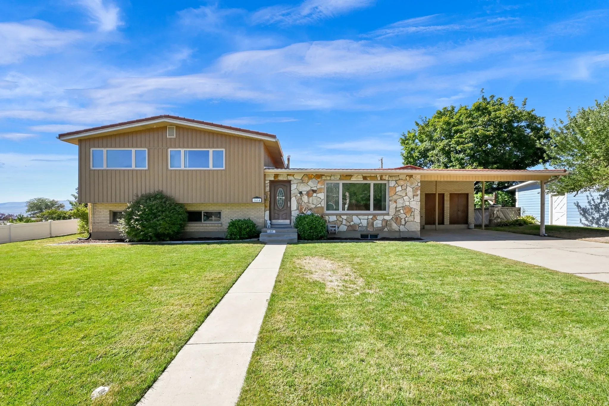 Split-level residence featuring a stone and siding facade, a covered carport, and an expansive front lawn