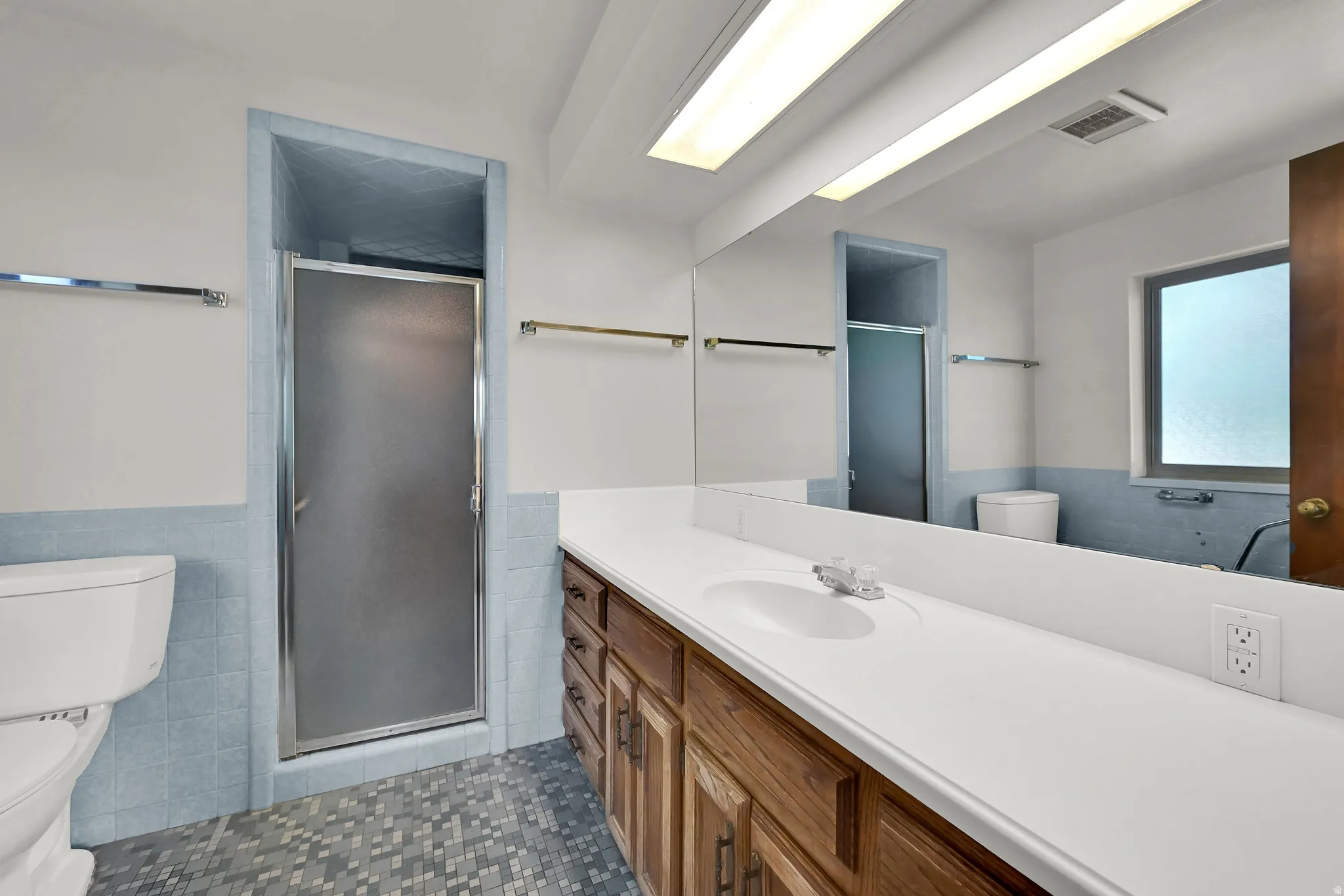 White vanity with a single sink, wood-finish cabinetry, and an expansive mirror
