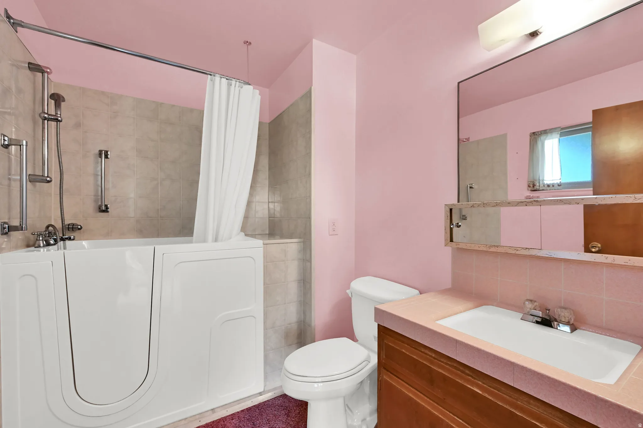 Walk-in tub with grab bars, tiled shower surround, built-in vanity with integrated sink, wall-mounted mirror, and overhead lighting fixture