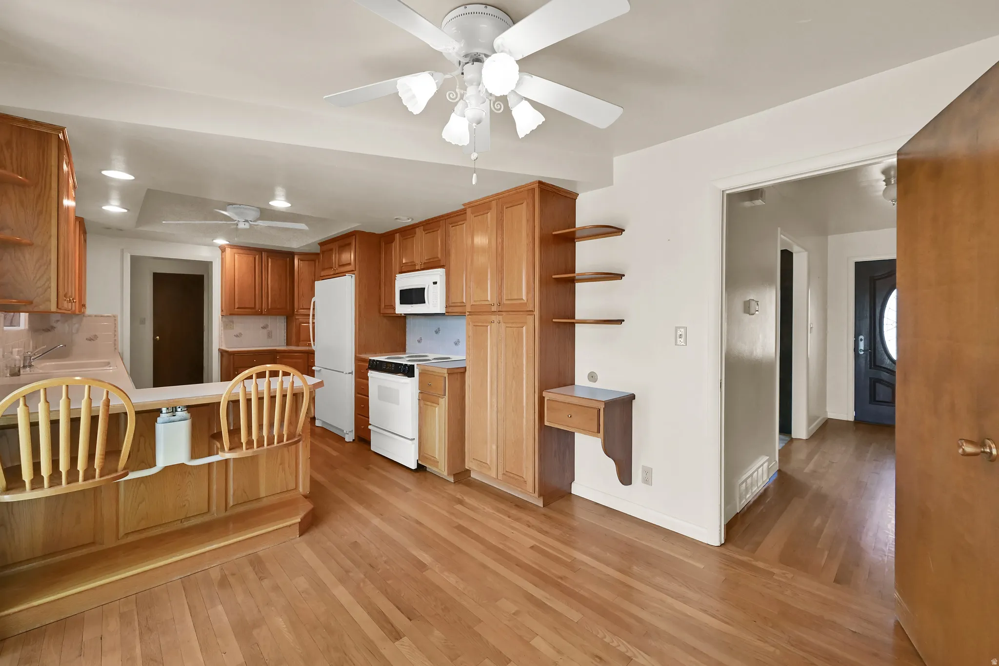 Kitchen with wood-finish flooring, wood cabinetry, white appliances, and a built-in breakfast bar