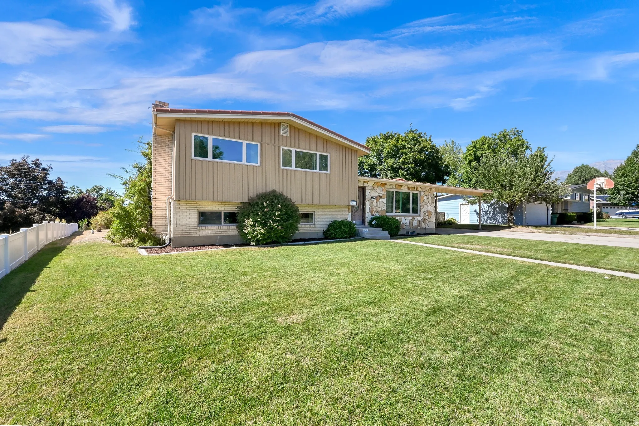 Two-story residence featuring a stone and siding exterior, a front lawn with a concrete walkway, and a white fence along the property line