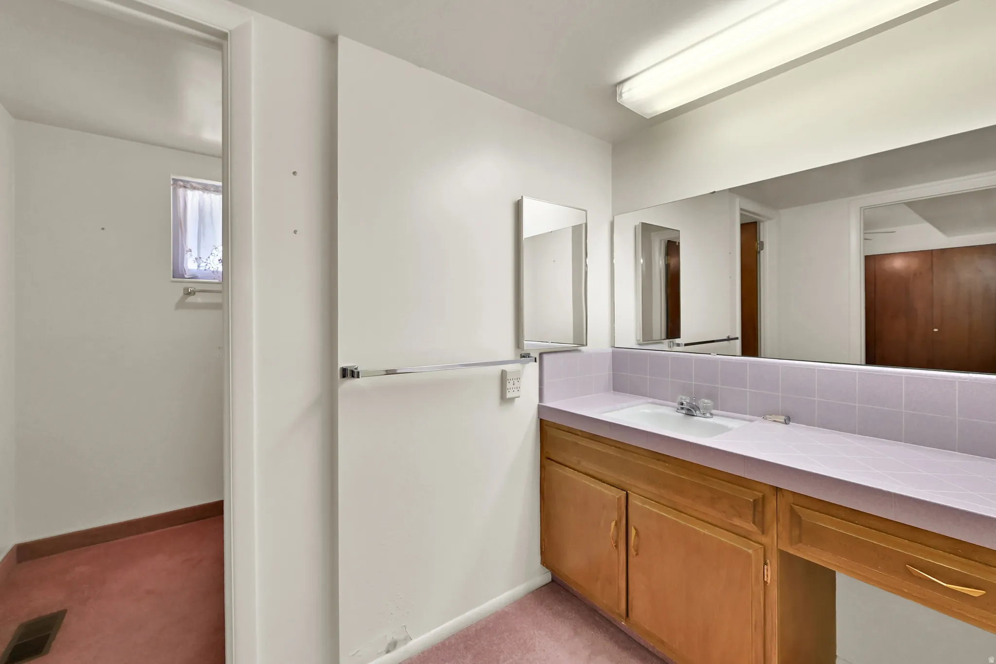 Built-in vanity with light wood cabinetry, integrated sink, and expansive mirror