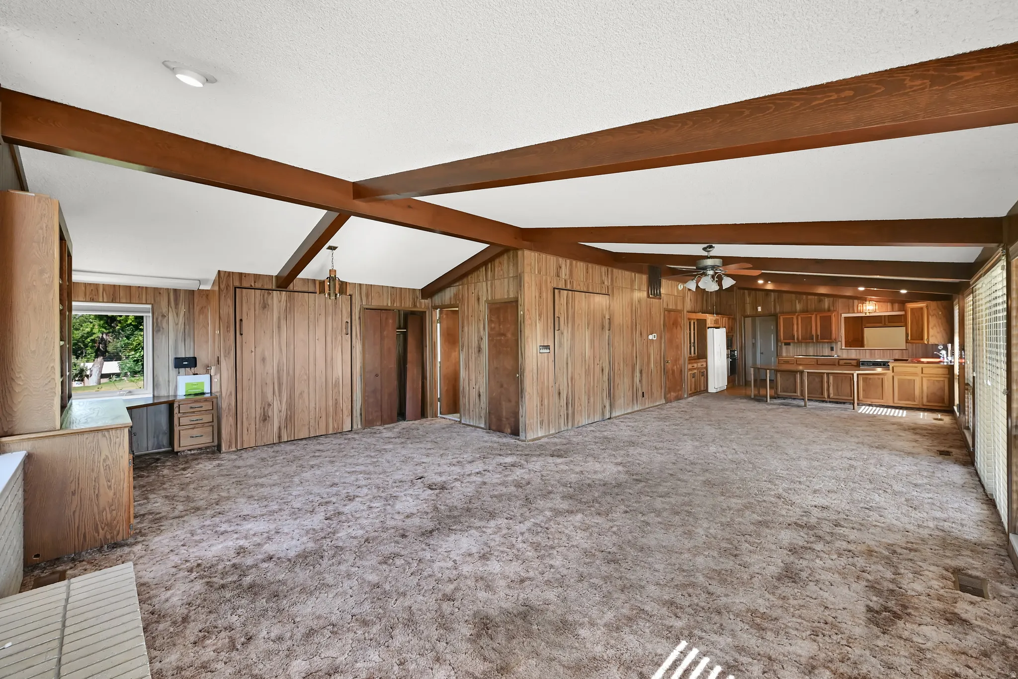 Vaulted ceiling with exposed wood beams, wood-paneled walls, built-in cabinetry, and integrated kitchen area