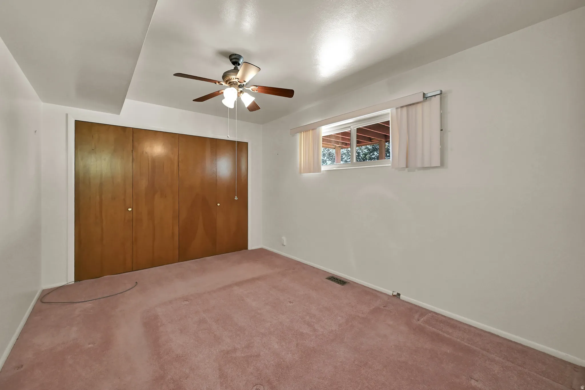 Wood-finish bi-fold closet doors, ceiling fan, carpeted flooring, and window with exterior natural light
