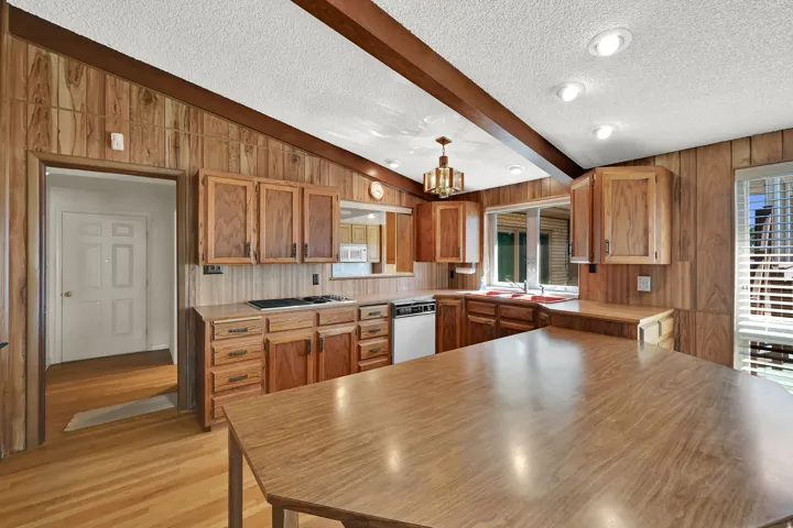 Kitchen featuring wood paneling, wood-finish flooring, wood cabinetry, a gas cooktop, and a kitchen island