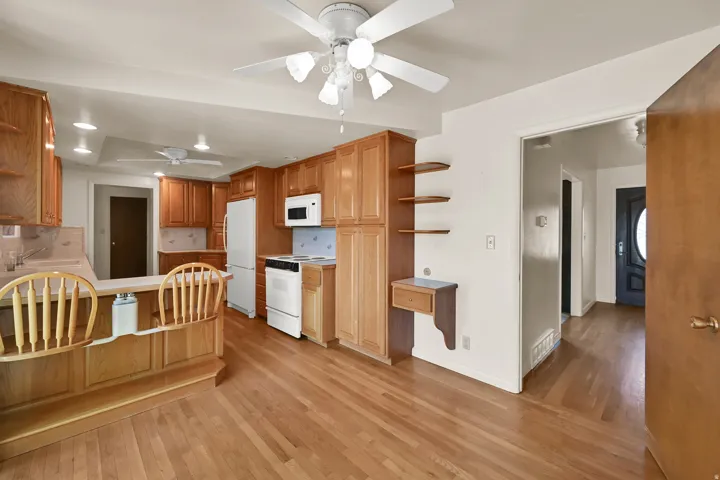 Kitchen with wood-finish flooring, wood cabinetry, white appliances, and a built-in breakfast bar