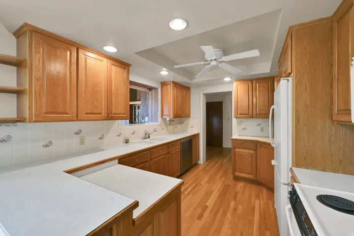 U-shaped kitchen featuring wood-finish cabinetry, white countertops, tile backsplash, and wood-finish flooring
