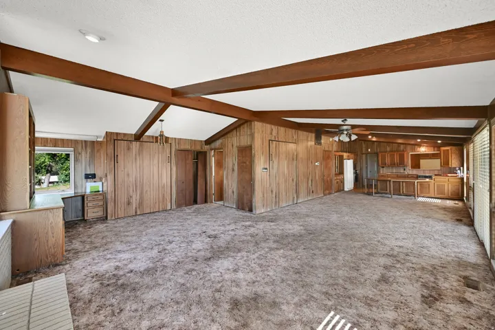 Vaulted ceiling with exposed wood beams, wood-paneled walls, built-in cabinetry, and integrated kitchen area