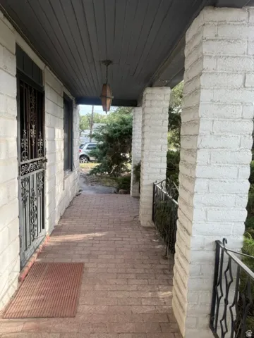 Covered porch with brick flooring, painted brick columns, decorative wrought iron railings, and a plank ceiling with a pendant light fixture